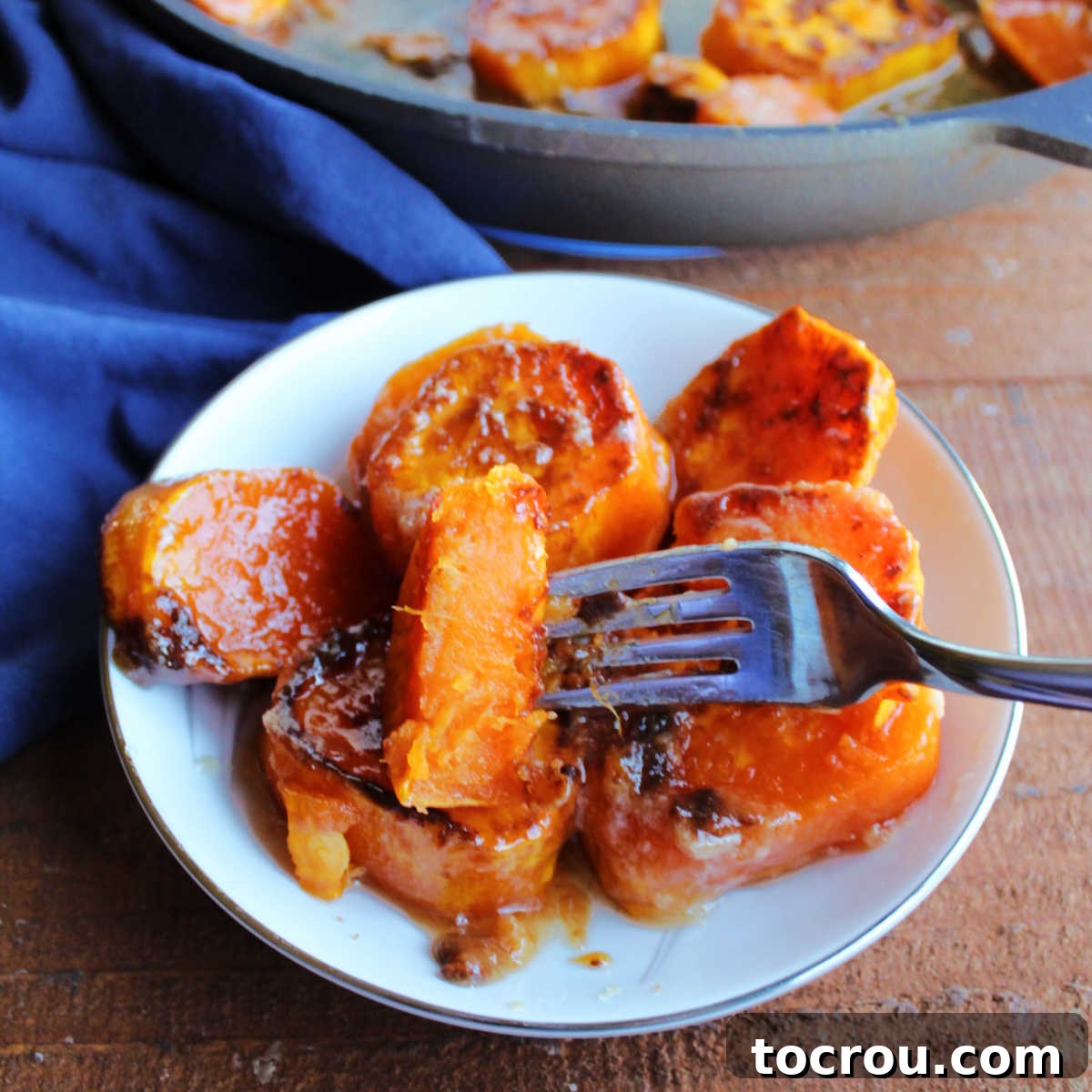 A perfectly cooked candied skillet sweet potato on a fork, showcasing its soft orange interior and sticky, glistening caramelized exterior.