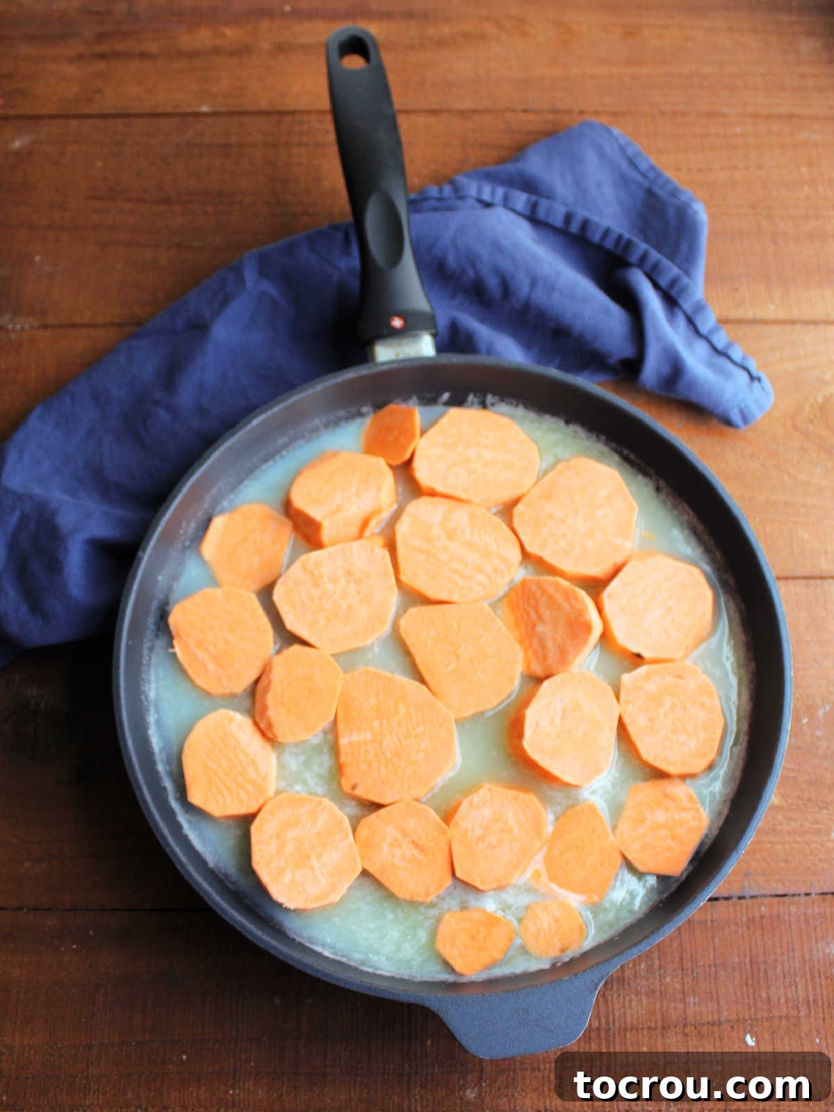 Thick, uniform slices of sweet potato arranged neatly in a skillet, submerged in a rich, simmering syrup, ready to be cooked.