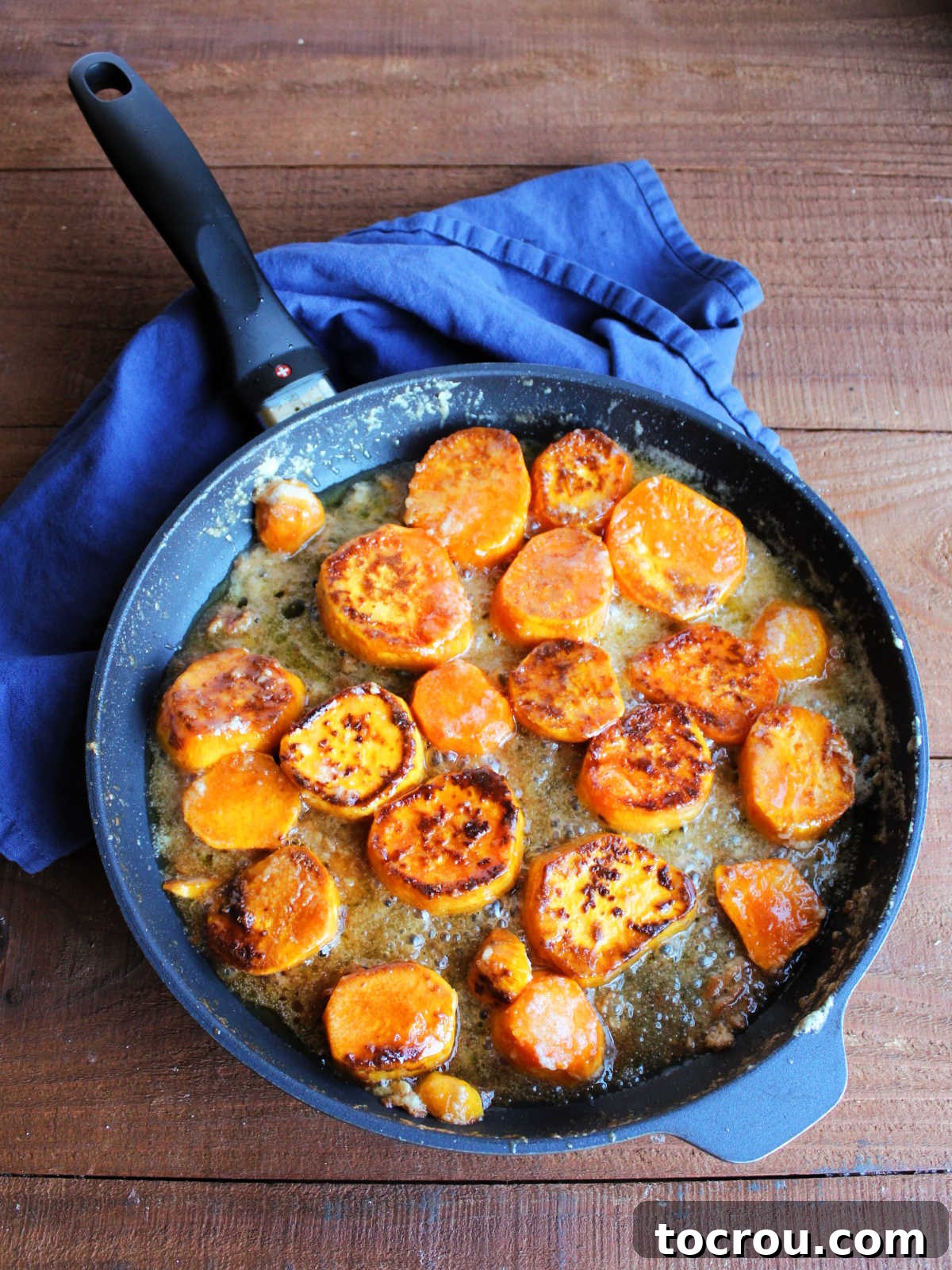 A skillet filled with perfectly cooked candied sweet potatoes, showcasing their beautiful browned and caramelized edges, with the reduced, sticky, and glossy sauce clinging to each piece.