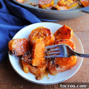 A close-up of a bite of skillet sweet potato on a fork, revealing its soft orange interior and invitingly sticky caramelized exterior.