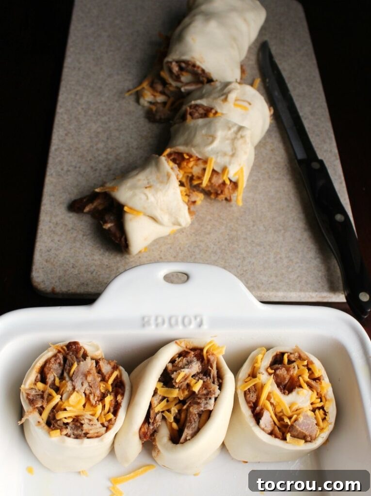 Rolled Pulled Pork Buns Before Rising Dough rolled around pork and cheese cut into cinnamon roll like slices with first few rolls in pan ready to rise.