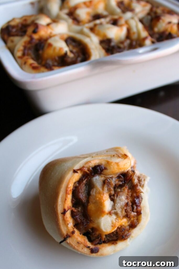 Baked Pulled Pork Bun on a Plate bbq pork and cheese stuffed roll on plate with pan in the background.