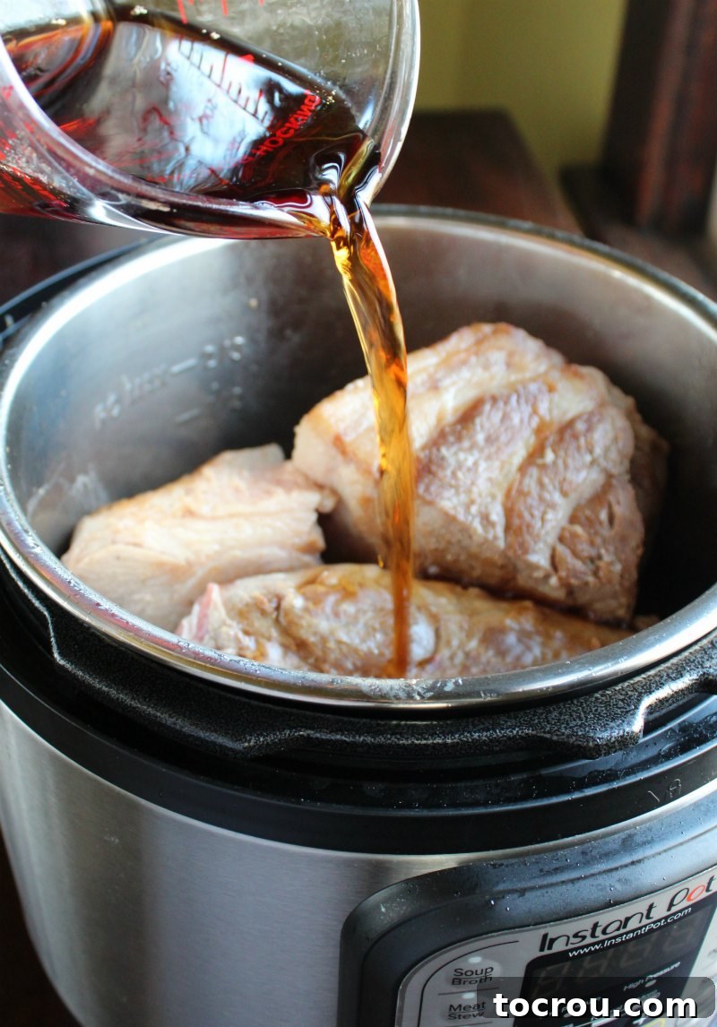 Pouring Root Beer into Instant Pot with Pork Chunks A hand pouring root beer directly over seasoned pork chunks in a pressure cooker.
