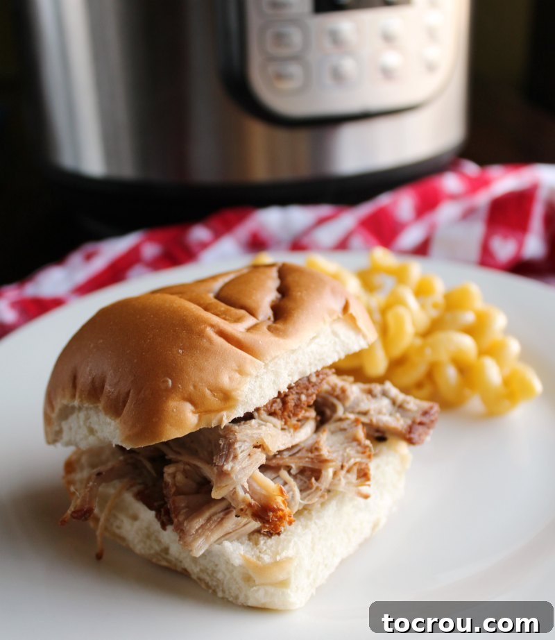Instant Pot Root Beer Pulled Pork Sandwich with Coleslaw Close-up of a root beer pulled pork sandwich topped with creamy coleslaw, with an Instant Pot blurred in the background.
