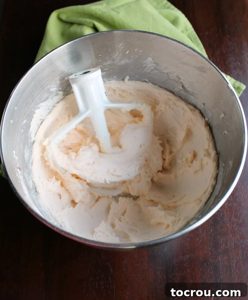 A stainless steel mixer bowl filled with a generous quantity of light, pastel peach-colored buttercream, perfectly whipped and ready for piping.