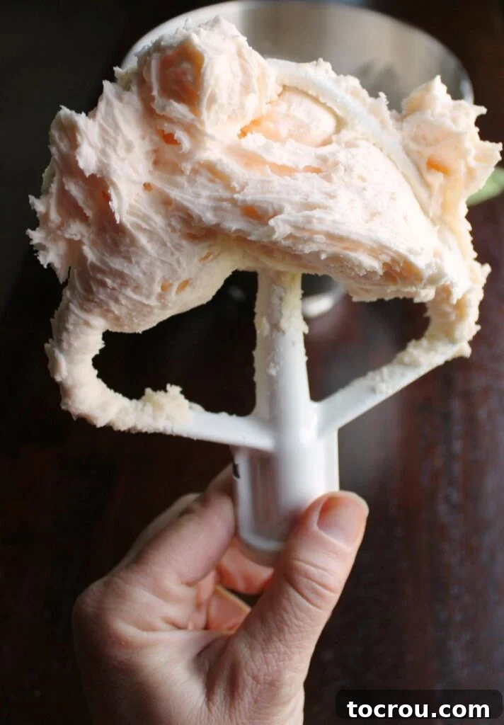 A mixer paddle coated with an ample amount of fluffy, smooth peach buttercream, showcasing its light and airy texture.