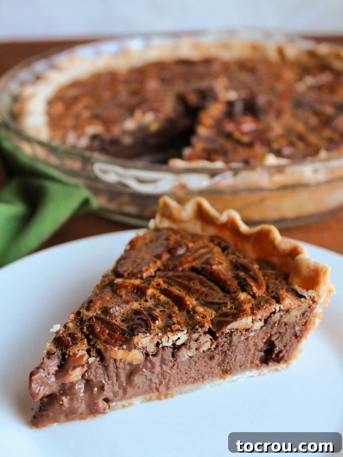 Slice of chocolate condensed milk pie on dessert plate with remaining pie in the background.