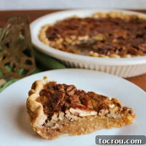 Slice of classic pecan pie with golden crust, gooey filling and lots of pecans on top.
