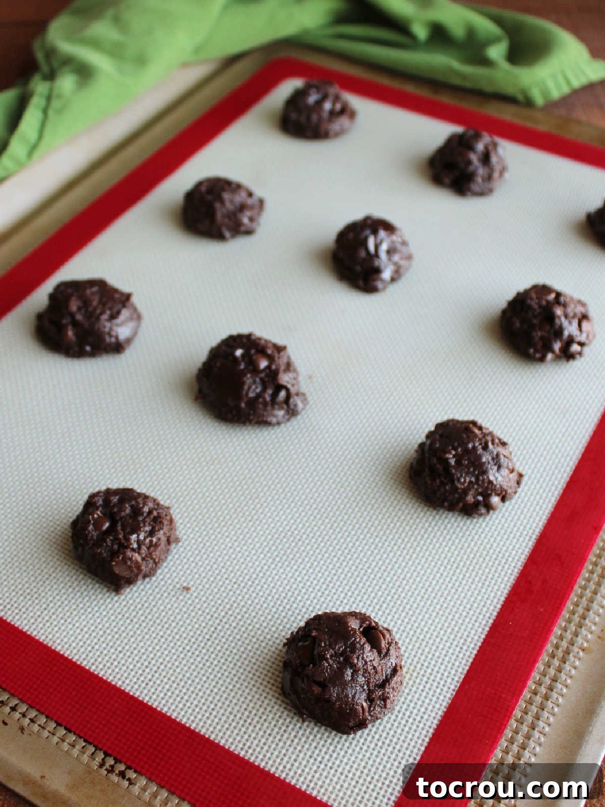 One-Bowl Brownie Cookies 7 Scoops of thick, unbaked brownie mix cookie dough arranged on a cookie sheet lined with a silicone mat, evenly spaced for baking.