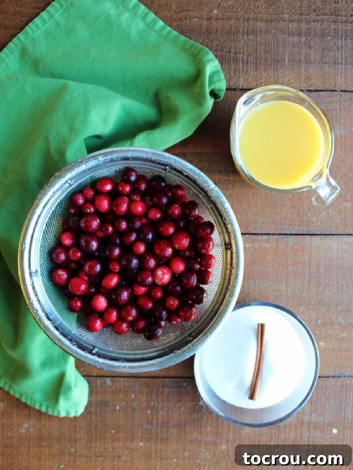 Ingredients including washed fresh cranberries, sugar, a cinnamon stick, and orange juice ready to be made into homemade cranberry sauce.