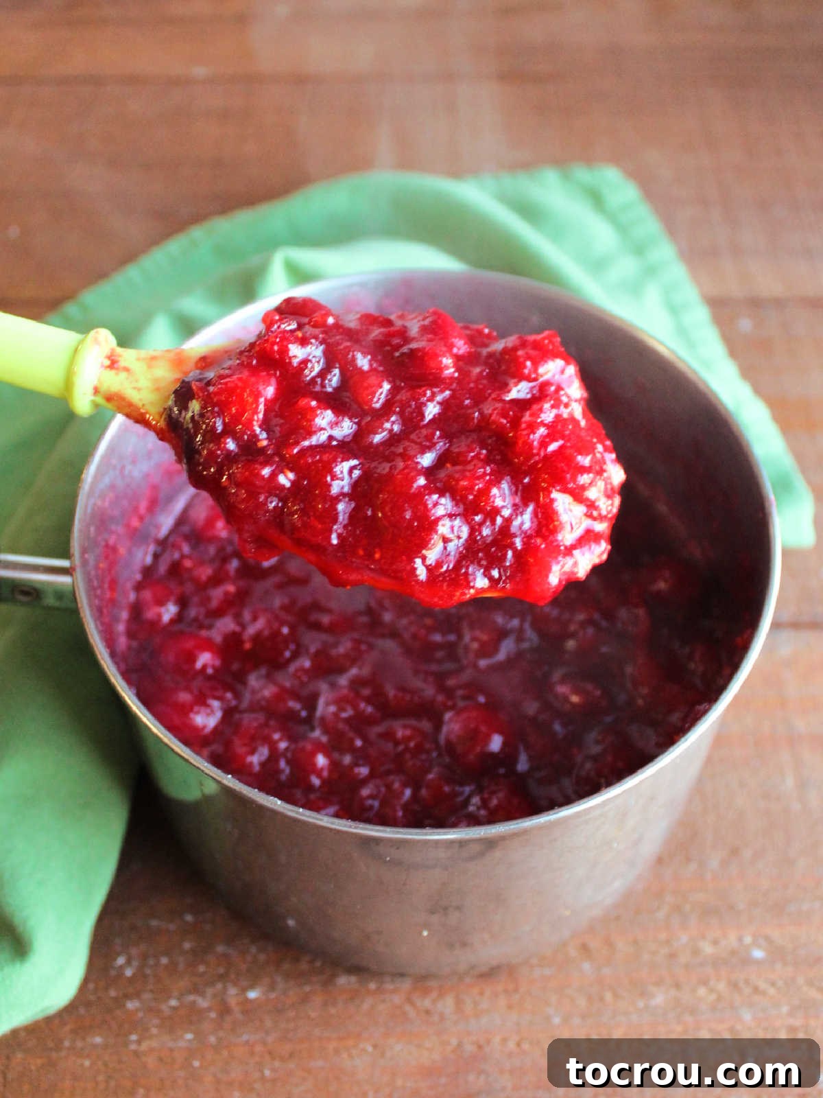 Large spoon with big scoop of hot cranberry sauce showing how the berries burst and the sauce thickened.