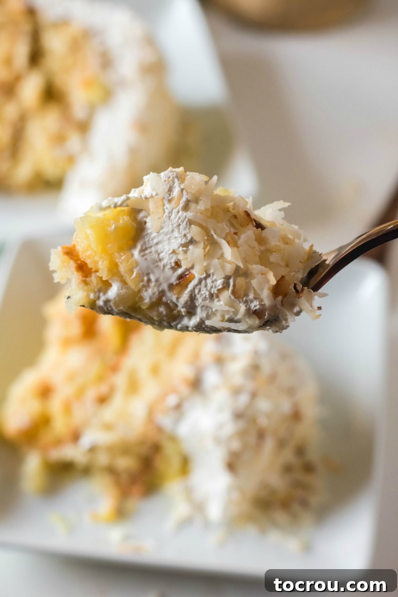 A delectable bite of Haleakala cake, revealing distinct layers of tender white milk cake, generous crushed pineapple filling, and airy fluffy white icing, crowned with toasted coconut.