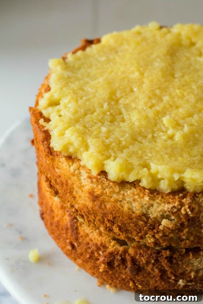 Layers of moist white cake and abundant pineapple filling stacked, ready to be covered with fluffy meringue frosting.