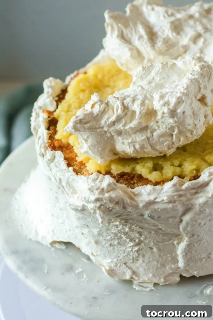 The process of applying fluffy white meringue frosting over the pineapple layer and soft white cake layers, creating a smooth, elegant finish.