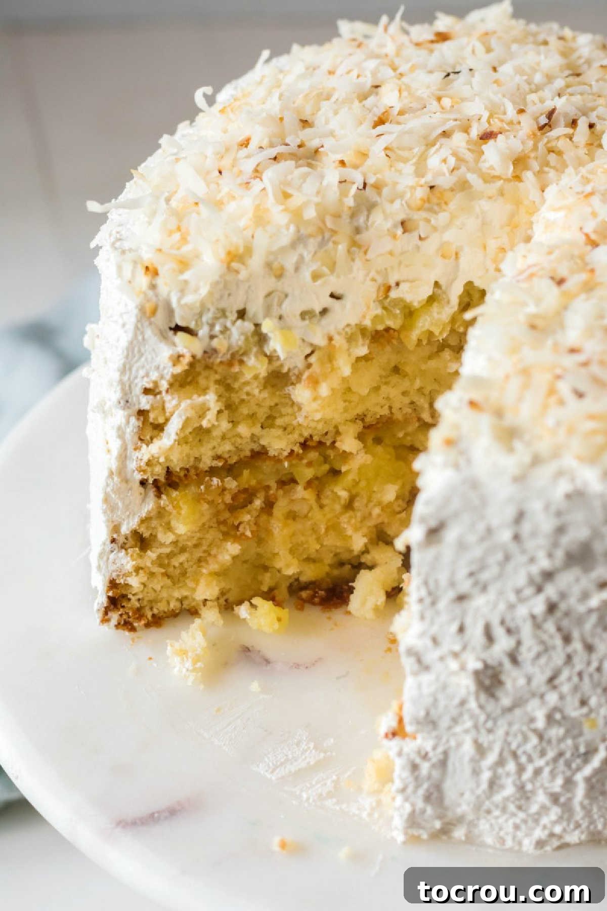 A perfect cross-section view of the Haleakala cake, distinctly showing its moist white cake layers, vibrant pineapple filling, fluffy white meringue frosting, and delicate toasted coconut topping.