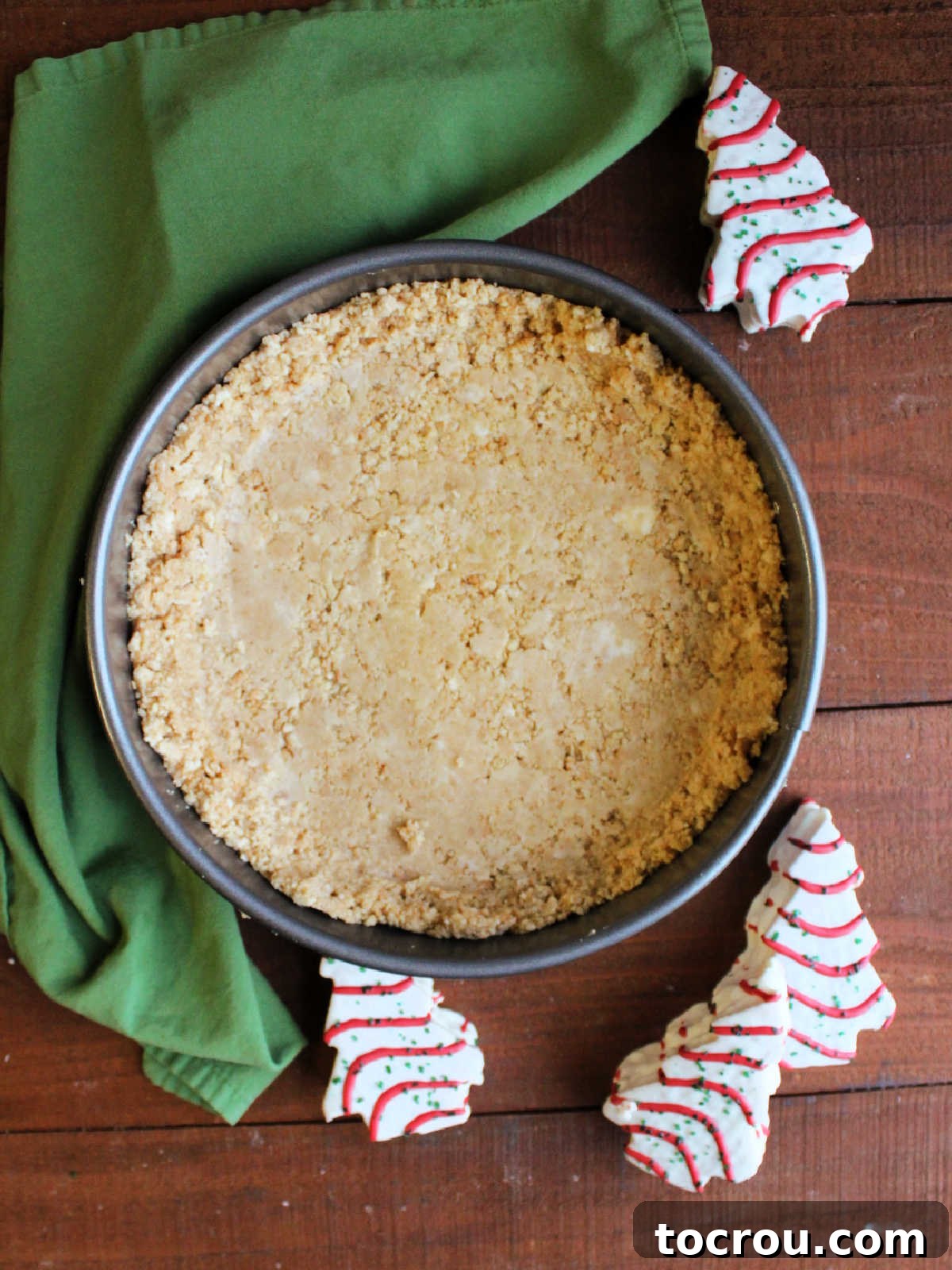 Golden Oreo crust in springform pan with Little Debbie Christmas tree cakes nearby.