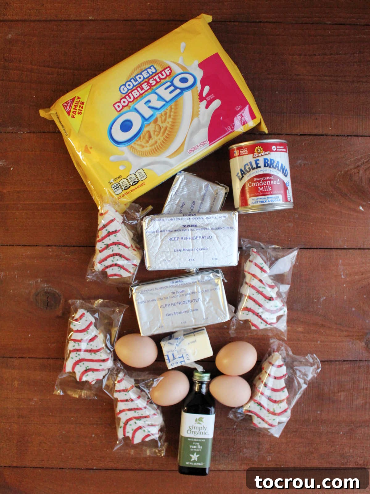 Ingredients including vanilla Oreos, sweetened condensed milk, cream cheese, eggs, vanilla, and Little Debbie Christmas tree snack cakes ready to be made into a cheesecake.