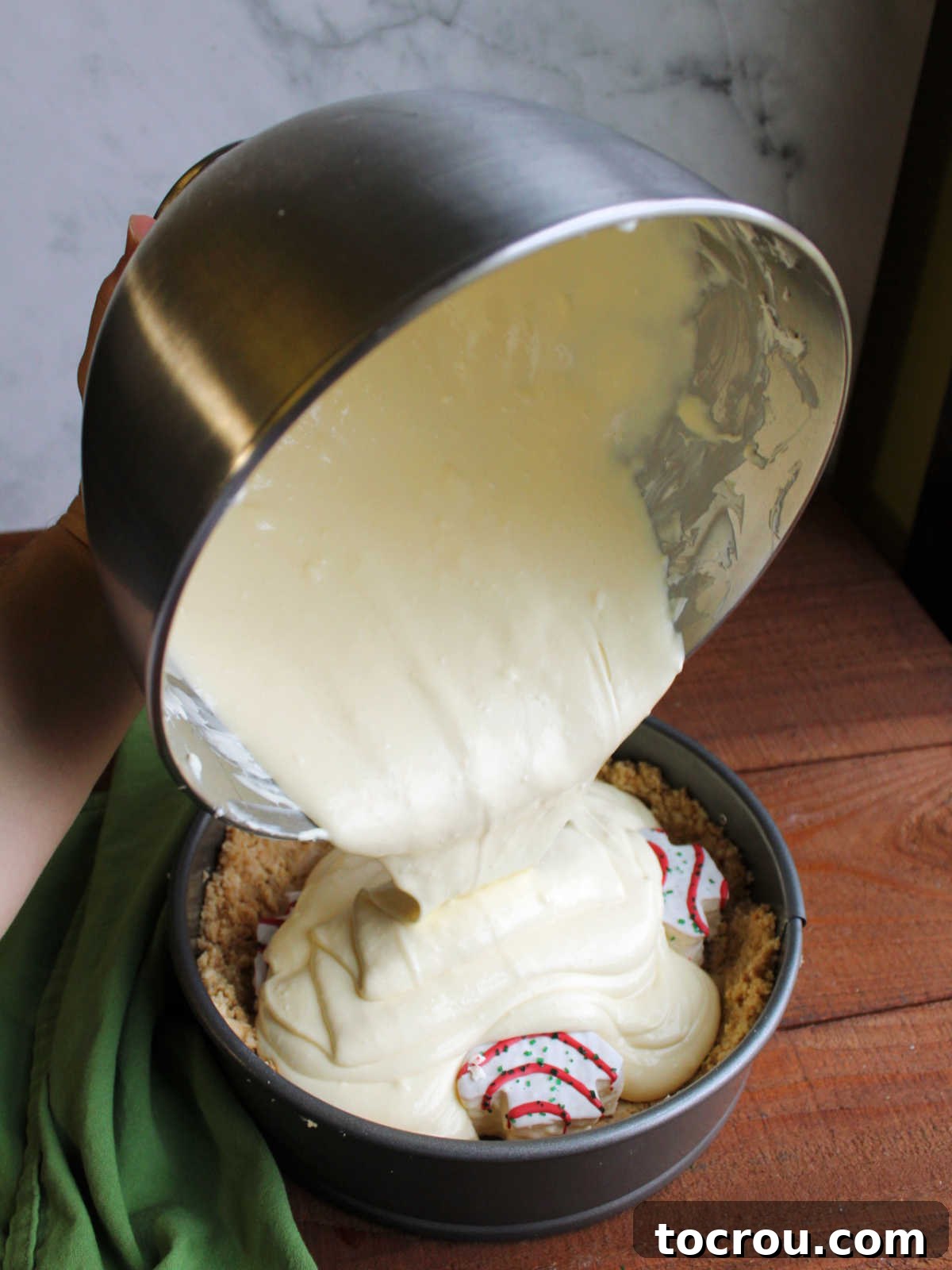 Pouring cheesecake batter over snack cakes and Oreo crust in springform pan.
