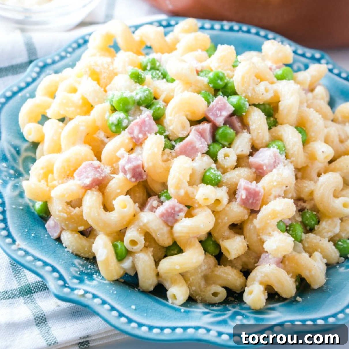 Creamy Pasta with Ham and Peas: The Ultimate Leftover Ham Recipe Close-up of a plate of curly pasta with generous cubes of ham, bright green peas, and a luscious Parmesan cheese sauce, inviting diners to indulge.
