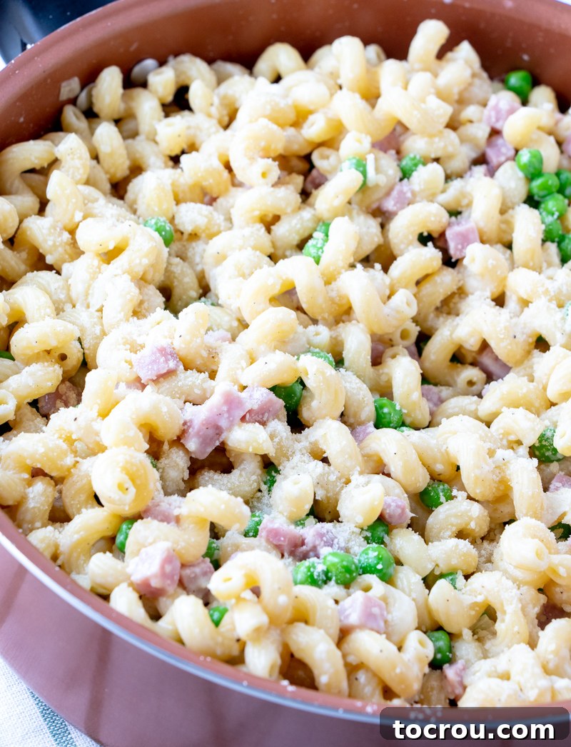 Sauté Pan of Creamy Ham and Pea Pasta Sauté pan brimming with perfectly cooked curly pasta, succulent chunks of ham, and vibrant green peas, all coated in a delicate, light cream sauce.