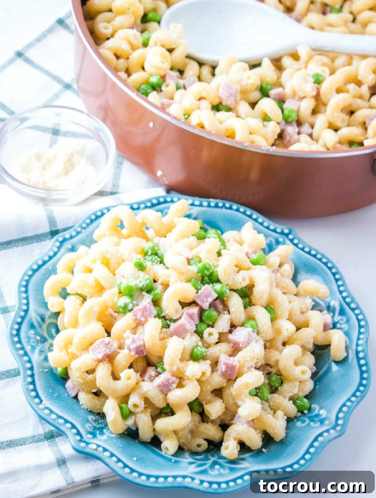 Creamy Ham and Pea Pasta Served A perfectly portioned plate of creamy pasta with ham and peas, served in front of the remaining pasta in the sauté pan, ready for more servings.