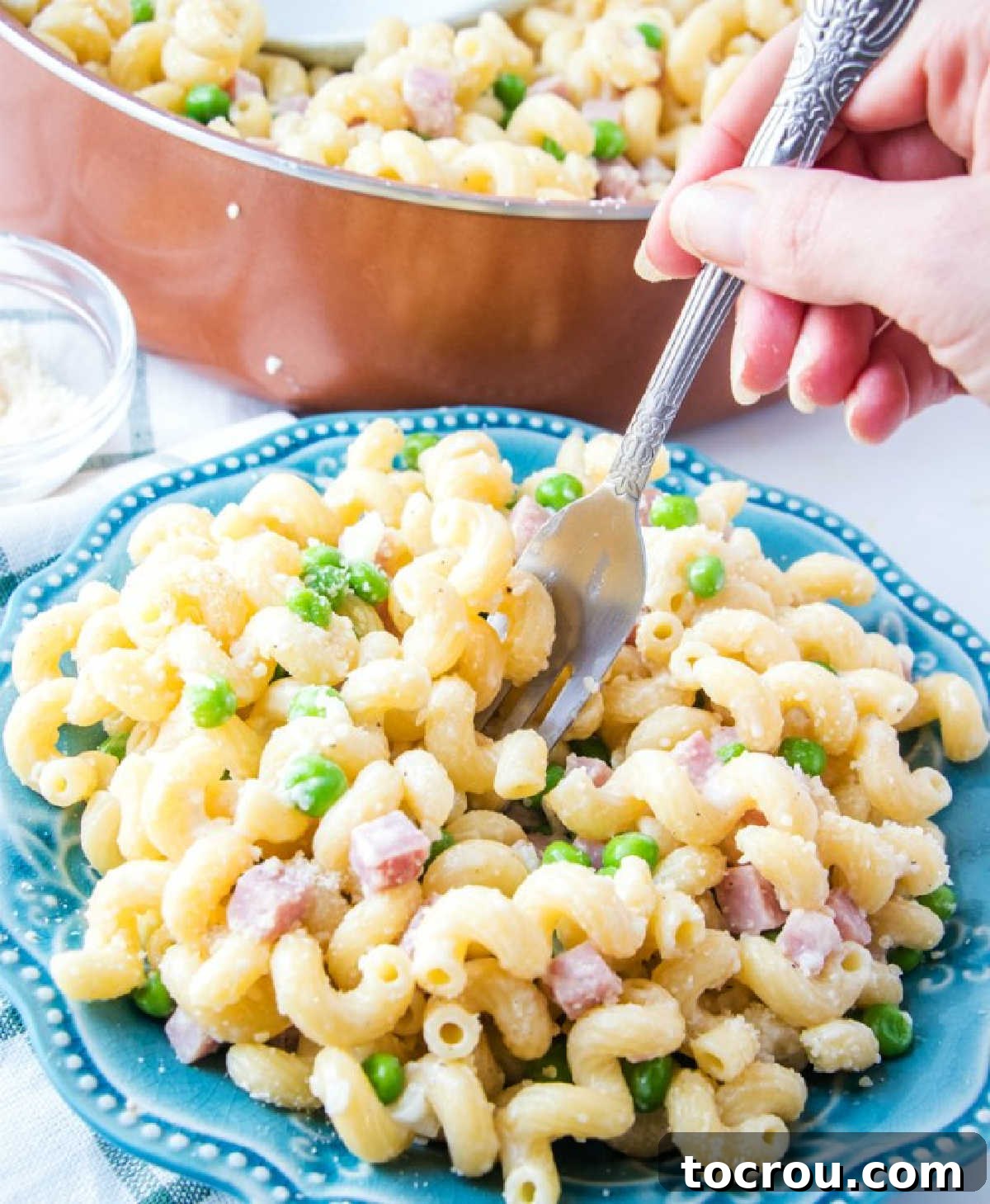 Enjoying Creamy Ham and Pea Pasta A fork lifts a generous bite of creamy pasta, ham, and peas, showcasing the perfect texture and sauce coating.