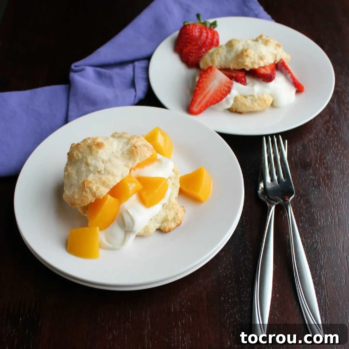 Two plates, one with a peach brunch shortcake and one with sliced strawberries and yogurt in a biscuit, garnished with fresh mint.