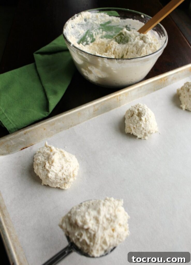 Bowl of biscuit dough and mounds of yogurt biscuit dough neatly arranged on a baking sheet, ready for the oven.