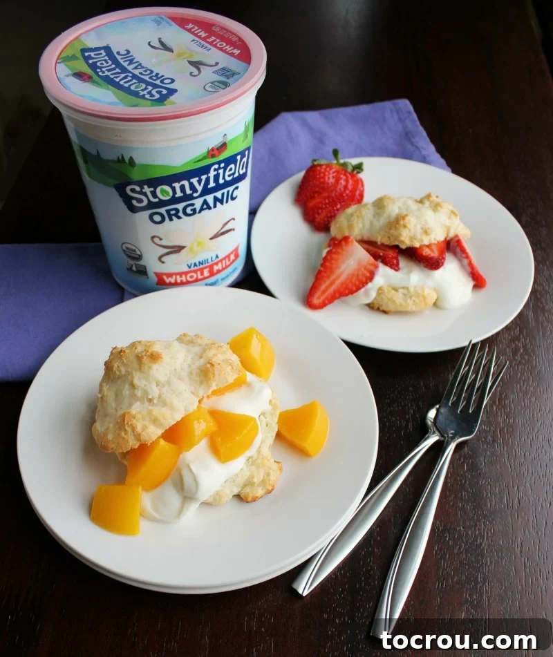 Plates of shortcakes filled with creamy vanilla yogurt, fresh peaches, and sliced strawberries, with a quart of Stonyfield yogurt in the background.