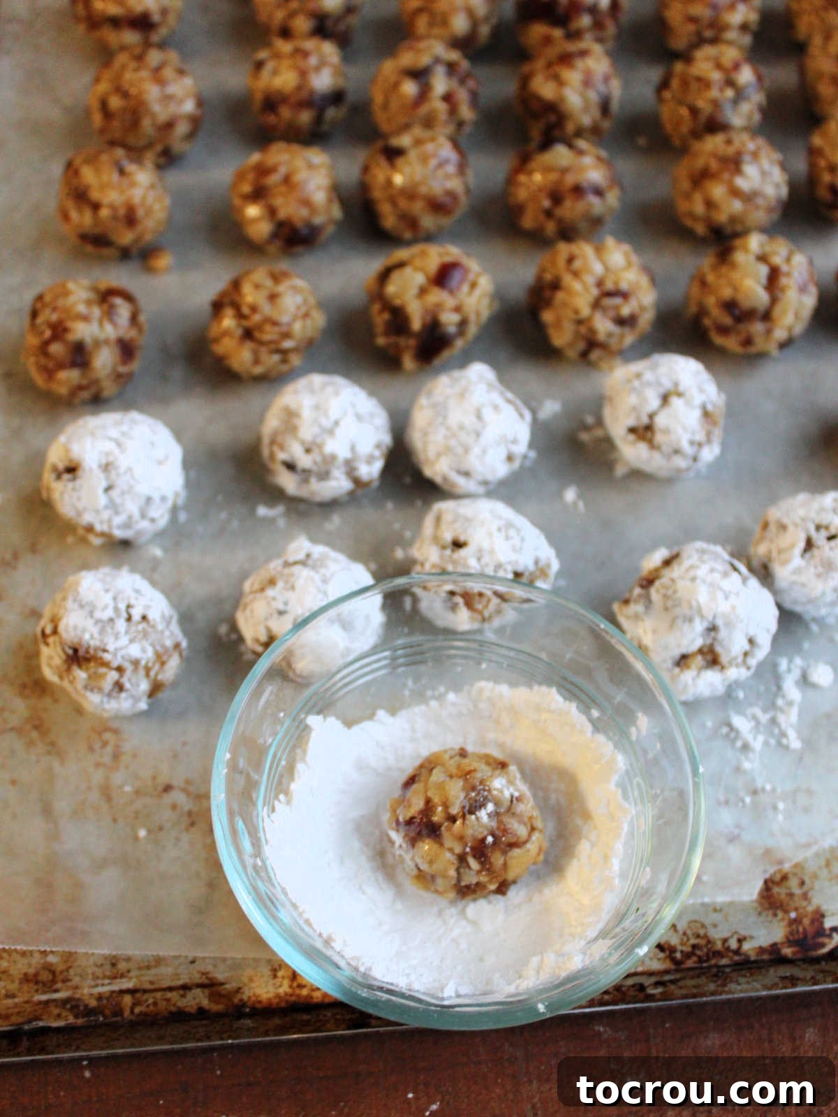 Grandma's Date Treats 9 Rolling date balls in a small bowl of powdered sugar.