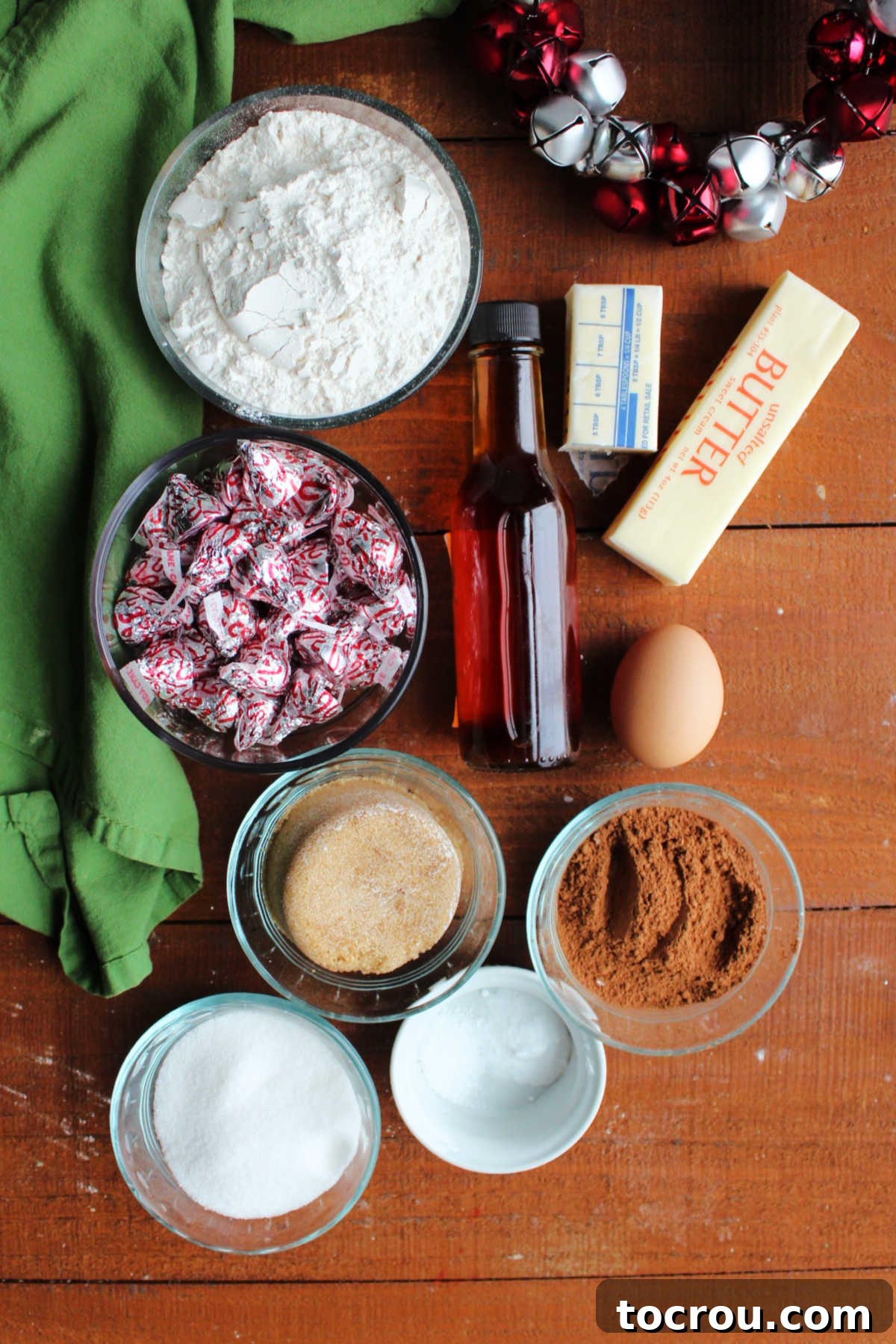 Peppermint Kissed Chocolate Blooms 4 A collection of ingredients laid out, including butter, egg, vanilla, cocoa powder, sugar, brown sugar, baking soda, salt, flour, and a bowl of candy cane Hershey's kisses, ready for baking.