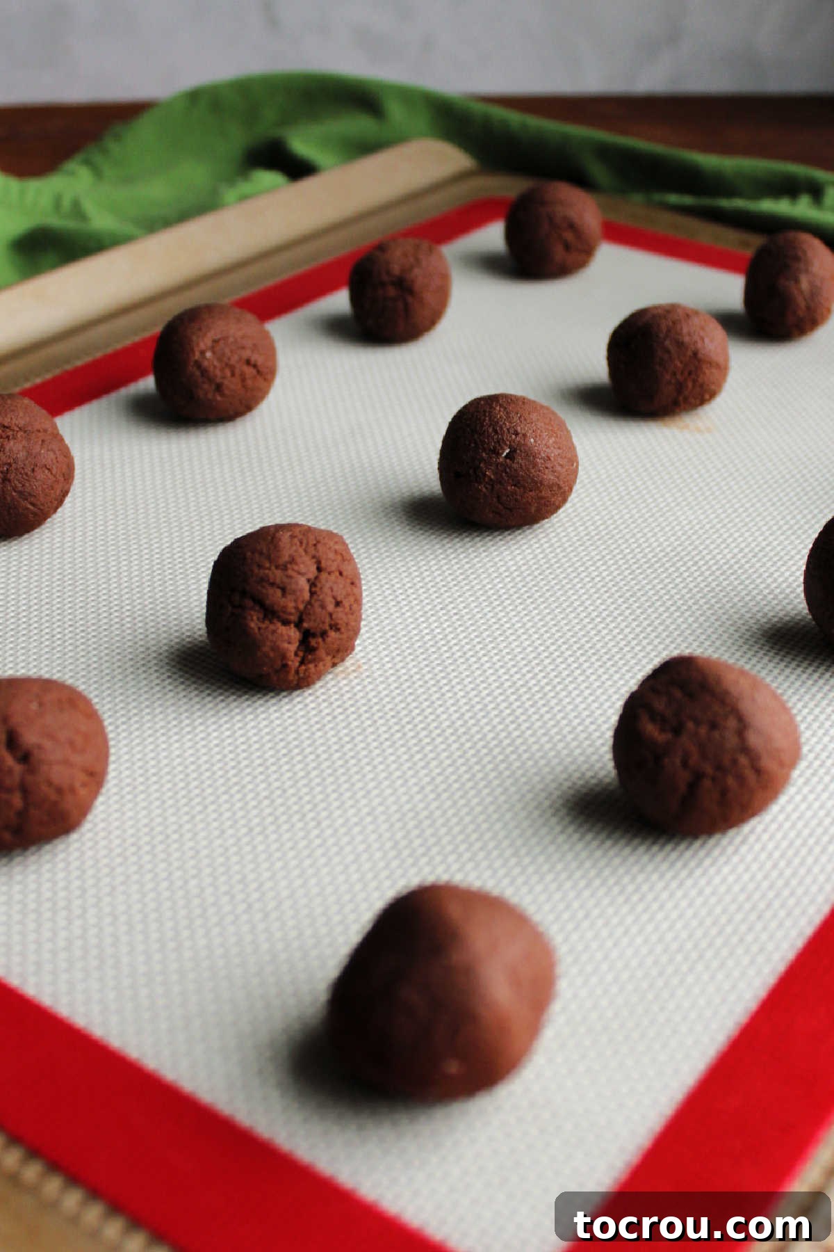 Peppermint Kissed Chocolate Blooms 6 Perfectly scooped balls of chocolate cookie dough arranged on a silicone mat lined cookie tray, ready for baking.