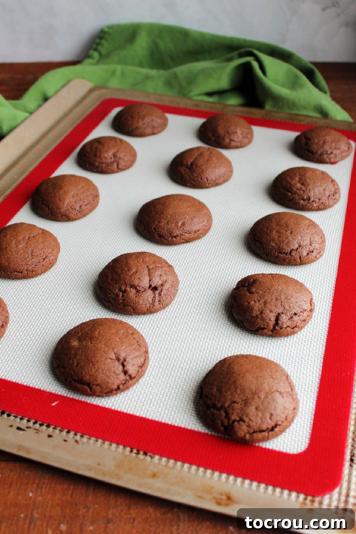 Peppermint Kissed Chocolate Blooms 7 Puffy, freshly baked chocolate cookies resting on a silicone mat lined cookie tray, perfectly golden and soft.