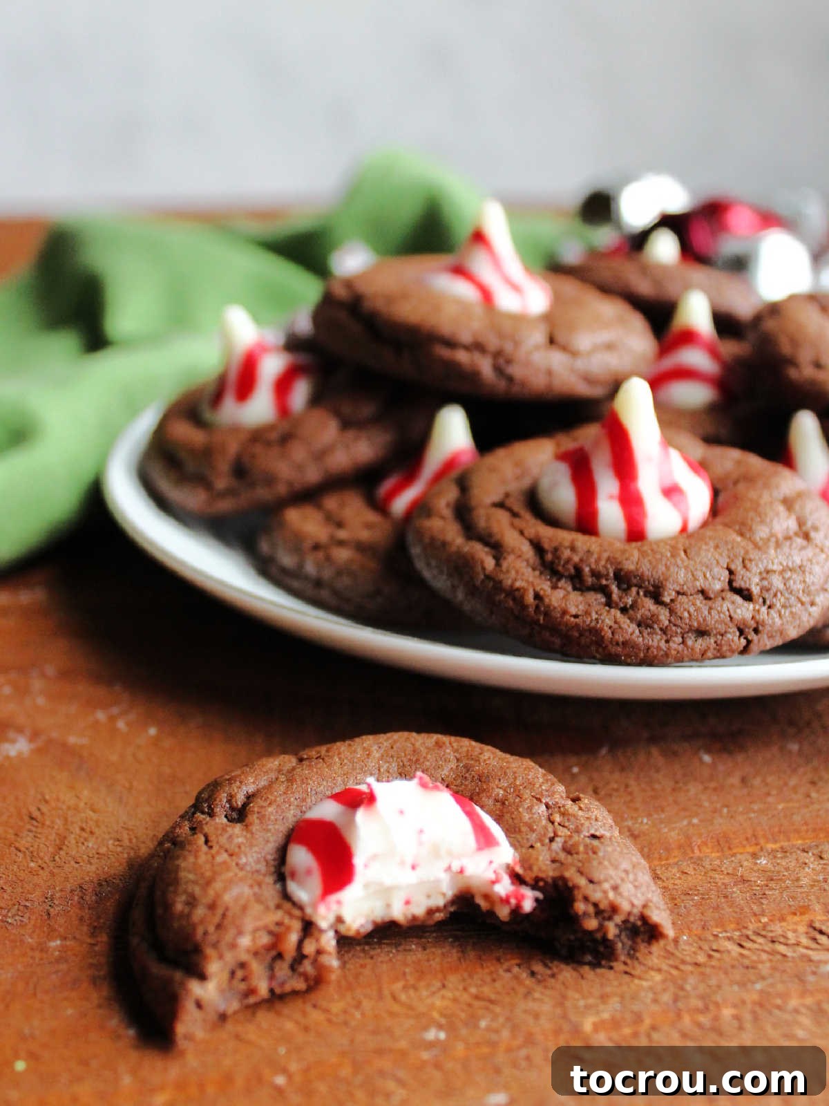 Peppermint Kissed Chocolate Blooms 10 A chocolate peppermint blossom cookie with a bite taken out, revealing its soft chocolate interior and the white chocolate peppermint Kiss center.