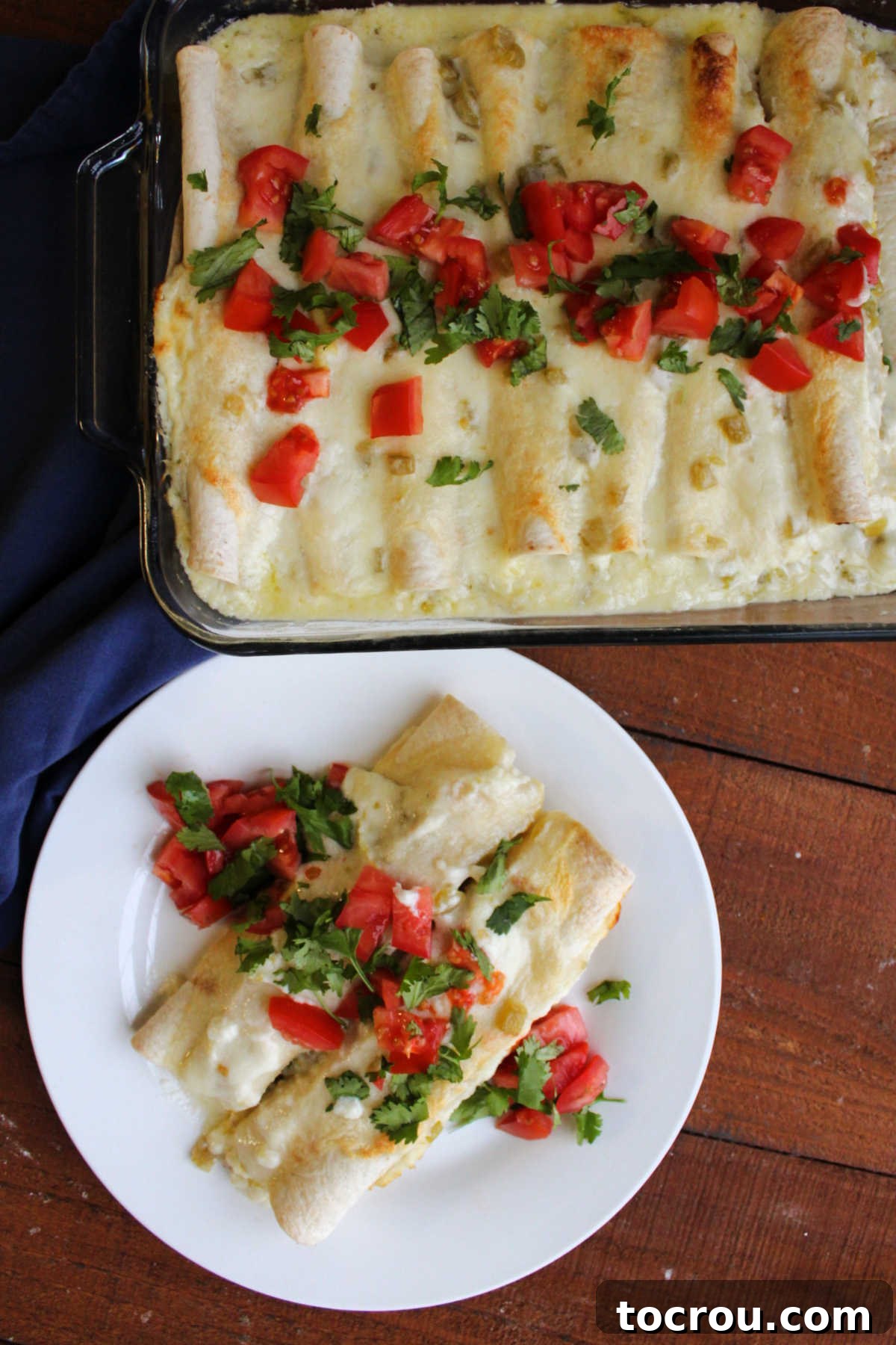 Pan of breakfast enchiladas next to a plate with two enchiladas topped with extra tomato and cilantro, ready to eat.