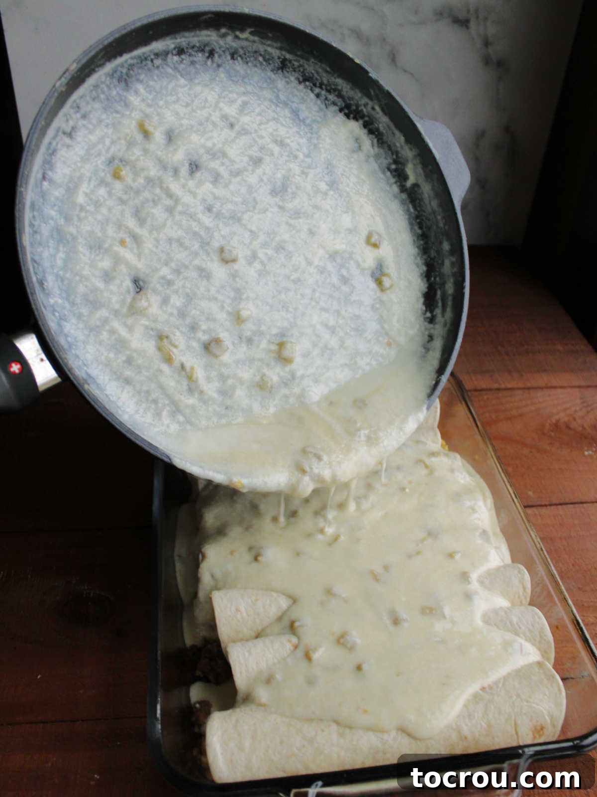 Pouring cheese sauce over enchiladas in baking dish, getting them ready to go in the oven.