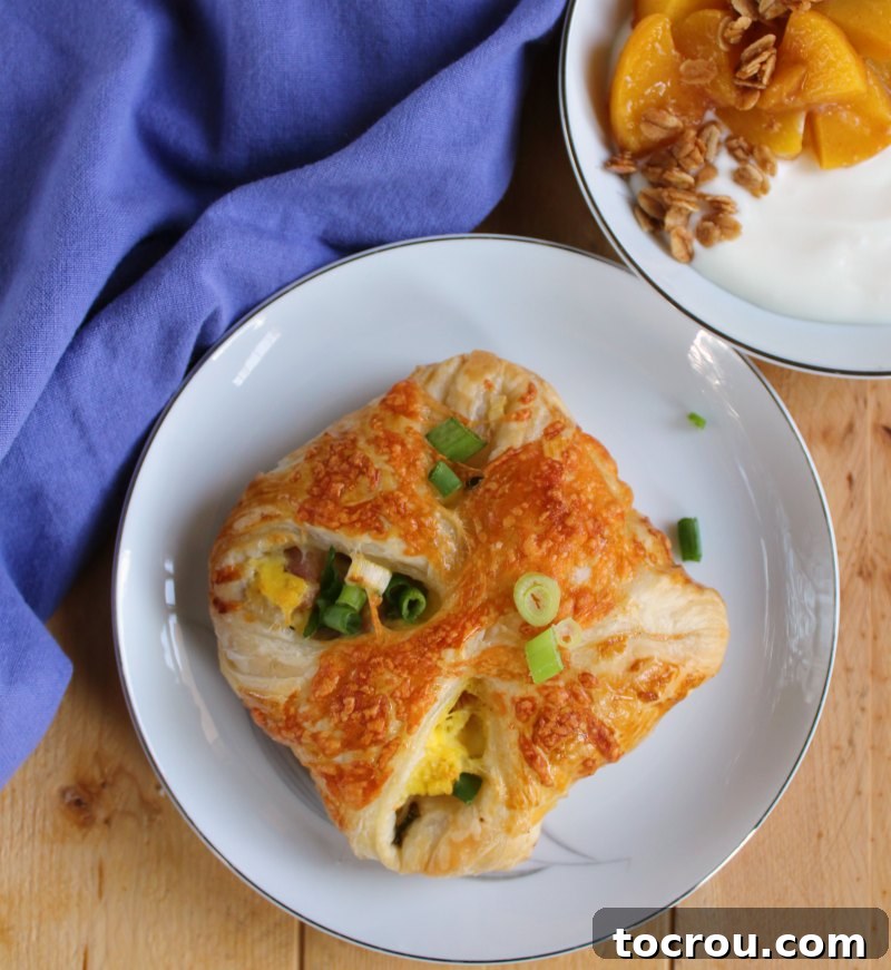 ham egg and cheese hand pie with scallions on top and a bowl of yogurt with peaches and granola in the background.