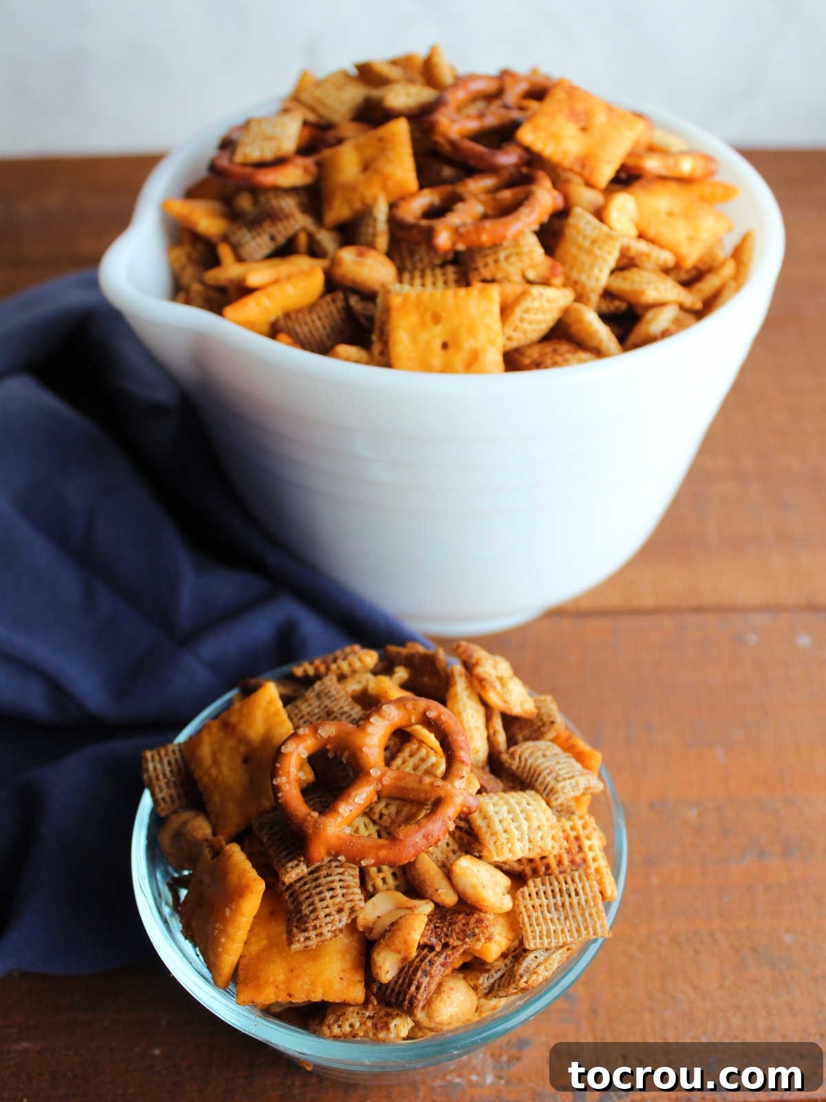 Larger white serving bowl filled with seasoned and smoked BBQ Chex mix next to a smaller bowl of Chex mix, ready to eat.
