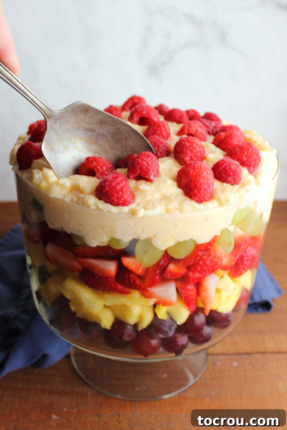 Antique berry spoon gracefully scooping a portion of layered fruit salad from a grand trifle bowl, showcasing the beautiful strata of fruits.