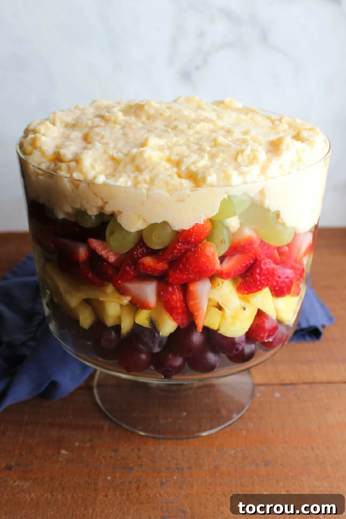 A thick, creamy layer of vanilla pudding mixture generously spread over a vibrant assortment of fresh fruits within a clear trifle bowl, creating a smooth, inviting transition.