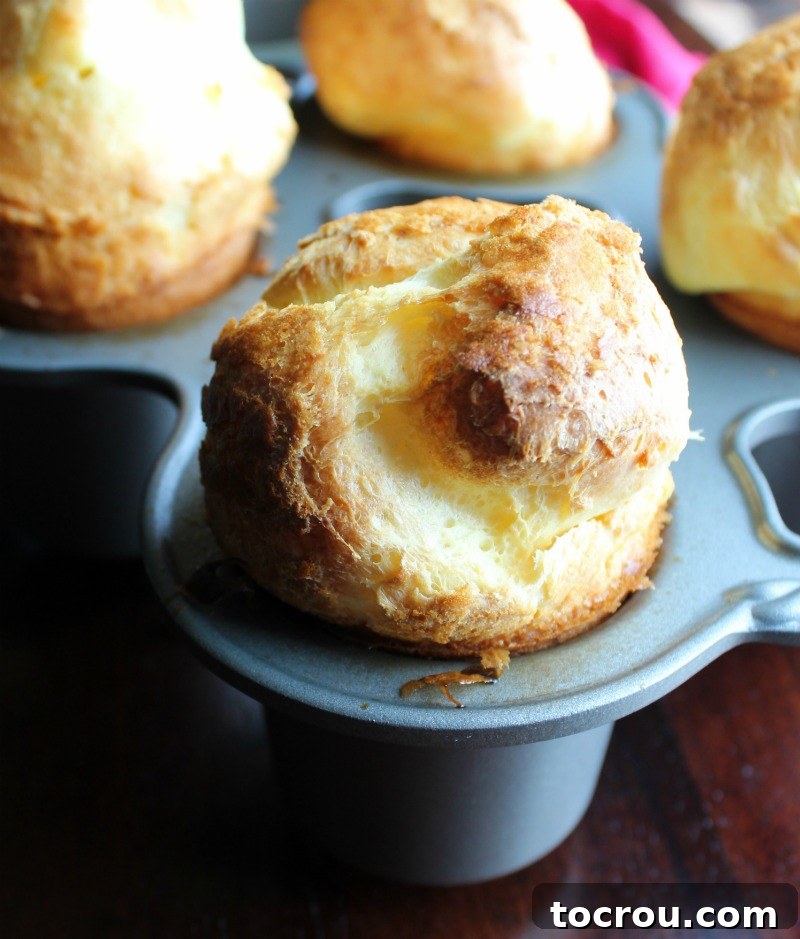 Freshly baked golden brown popover ballooning above a popover pan, showcasing its impressive rise and airy texture.
