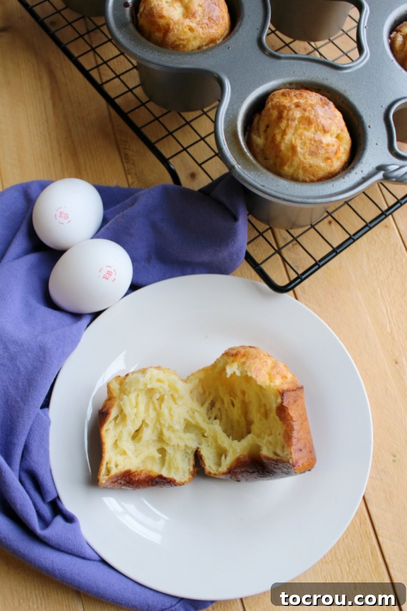 A freshly baked white cheddar popover on a plate, with Eggland's Best eggs and a Nordic Ware popover pan visible in the soft-focused background.
