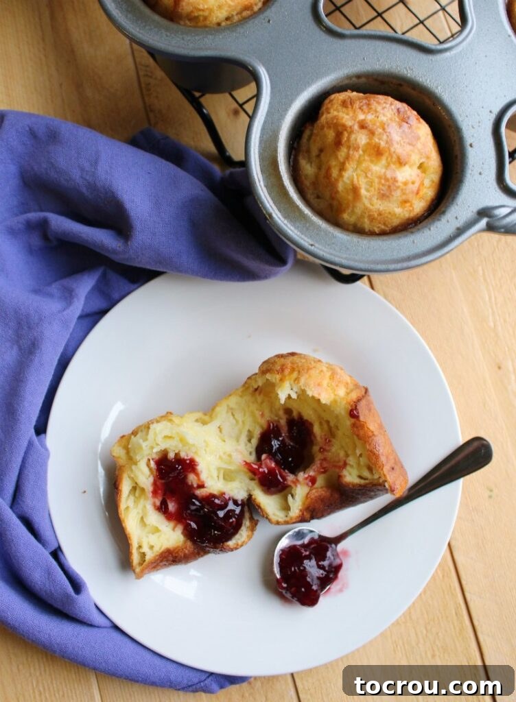 The fluffy interior of a white cheddar popover, topped with a spoonful of vibrant raspberry preserves.