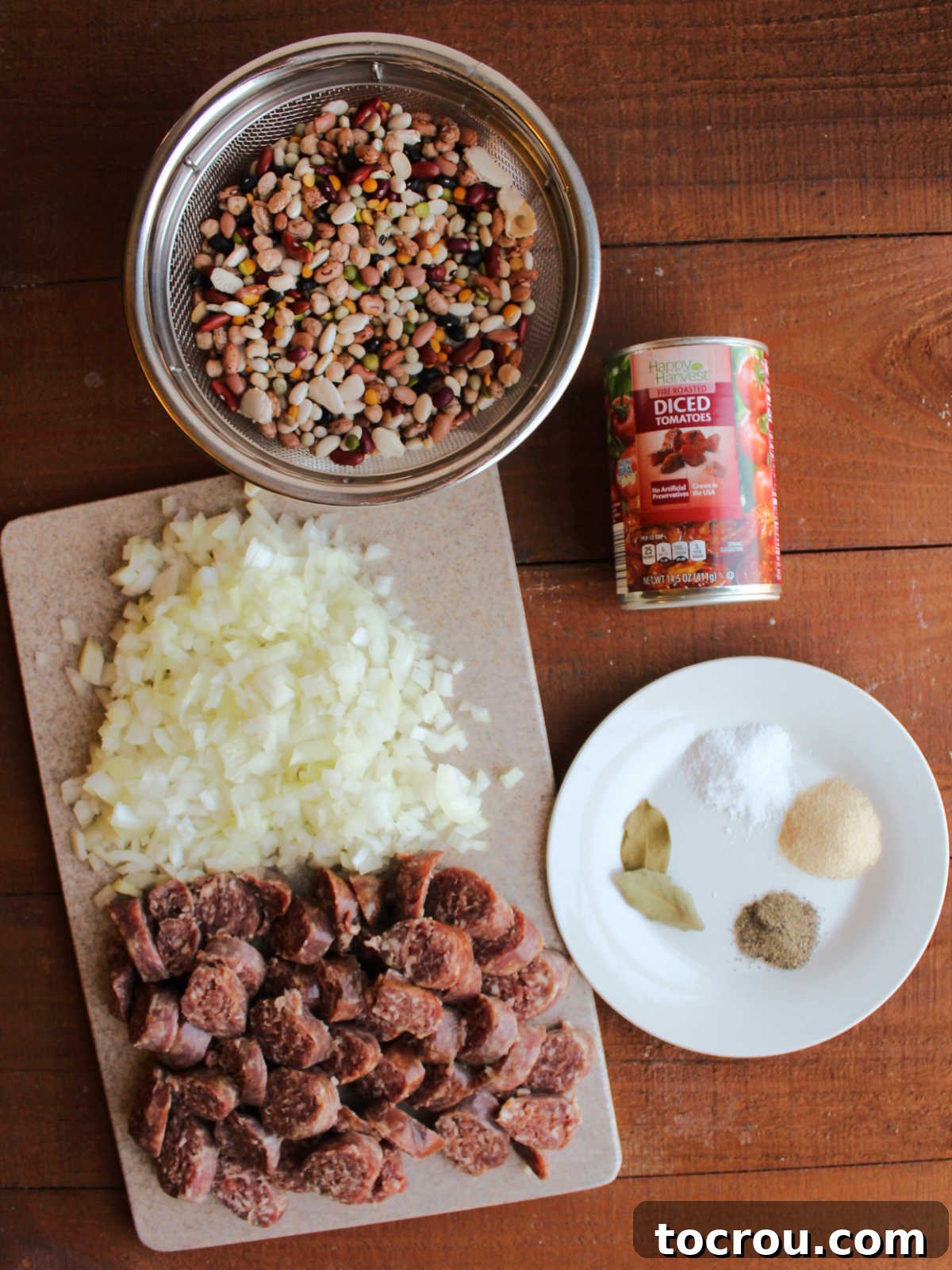 A collection of ingredients arranged for Instant Pot bean soup: a bowl of rinsed 16-bean mix, a diced onion, neatly sliced smoked sausage, various seasonings, and a can of fire-roasted diced tomatoes.