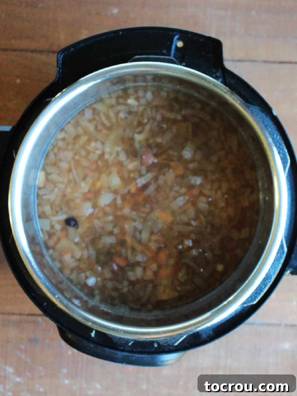 The Instant Pot inner pot filled with mostly cooked bean soup, showing softened beans in a simmering broth, awaiting the addition of sausage and tomatoes for the final cooking stage.