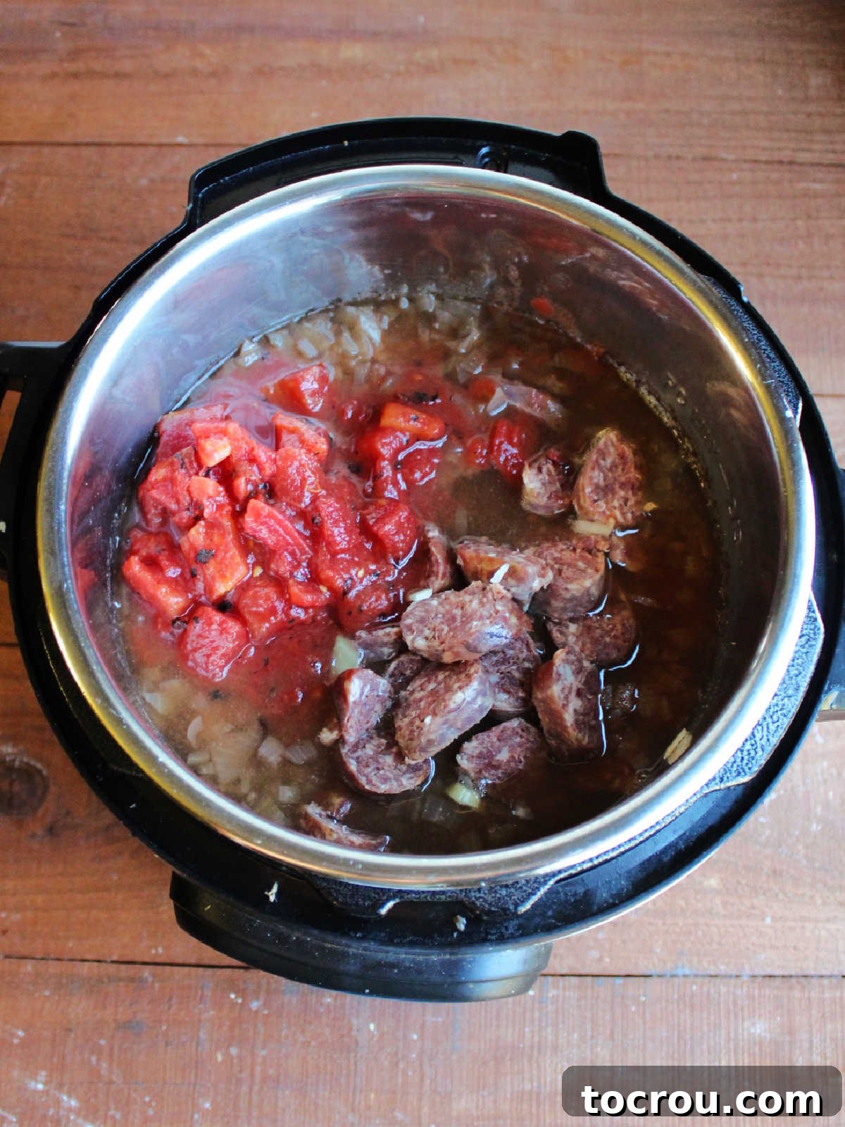 The Instant Pot inner pot, now holding cooked bean soup, ready for the final additions of diced tomatoes and thinly sliced kielbasa before a brief final cooking stage.
