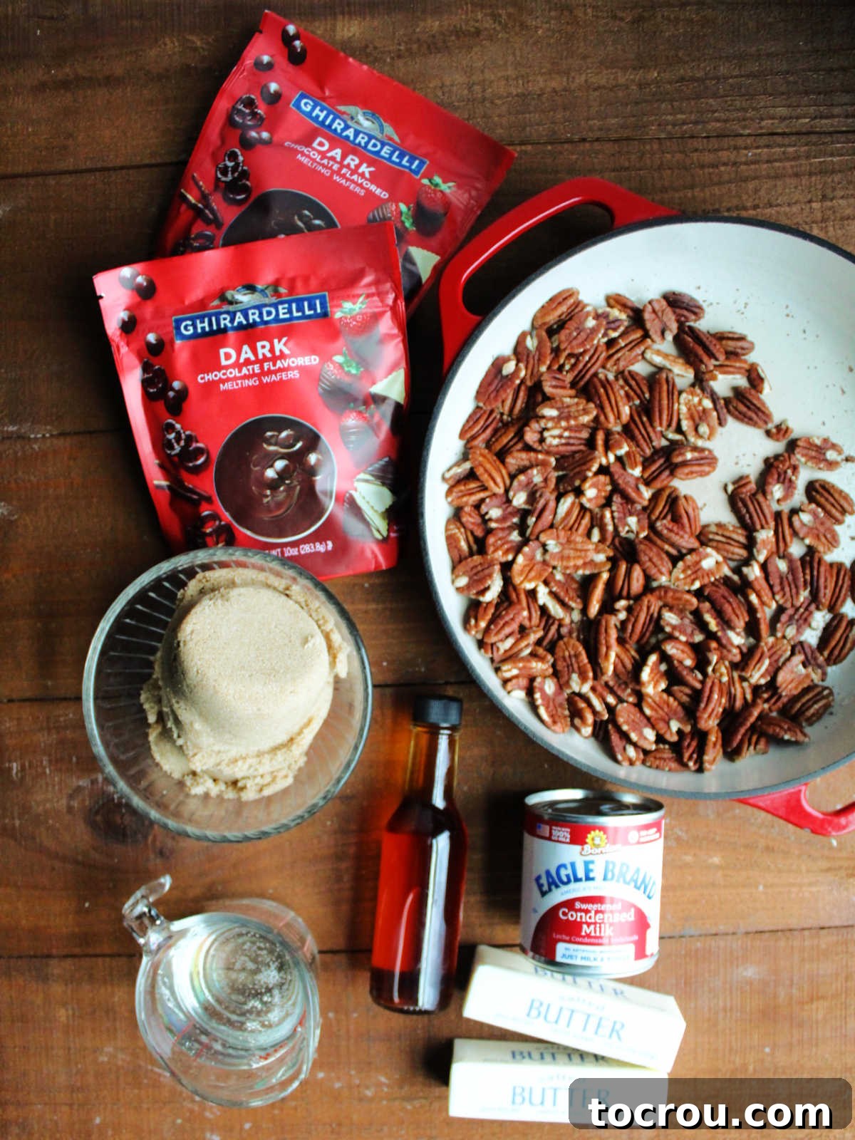 Ingredients including toasted pecans, sweetened condensed milk, butter, vanilla, corn syrup, brown sugar, and dark melting chocolate wafers ready to be made into turtle candies.