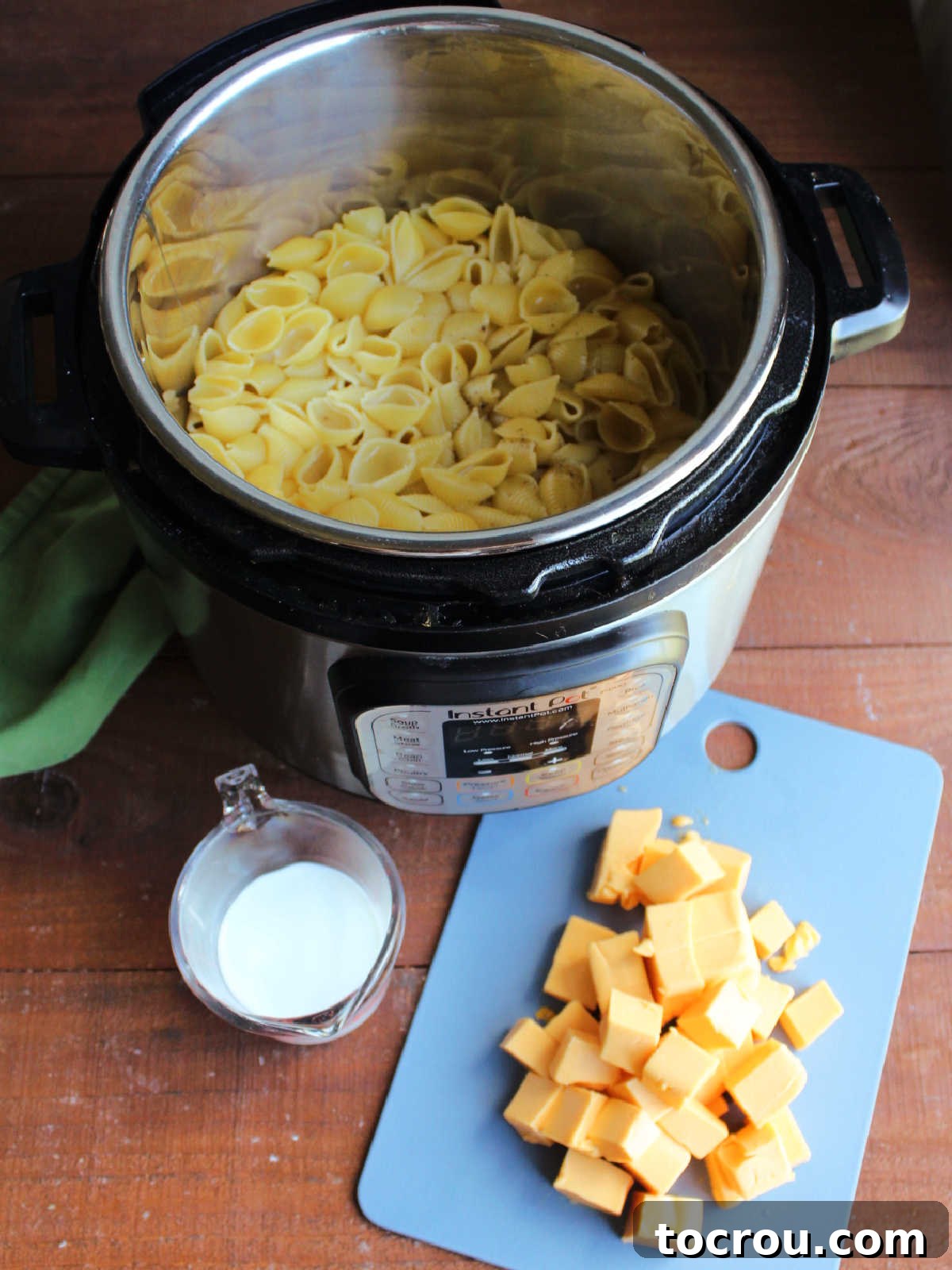 Instant Pot with cooked shell pasta in it with milk and cubed Velveeta nearby, ready to go in the pot. 