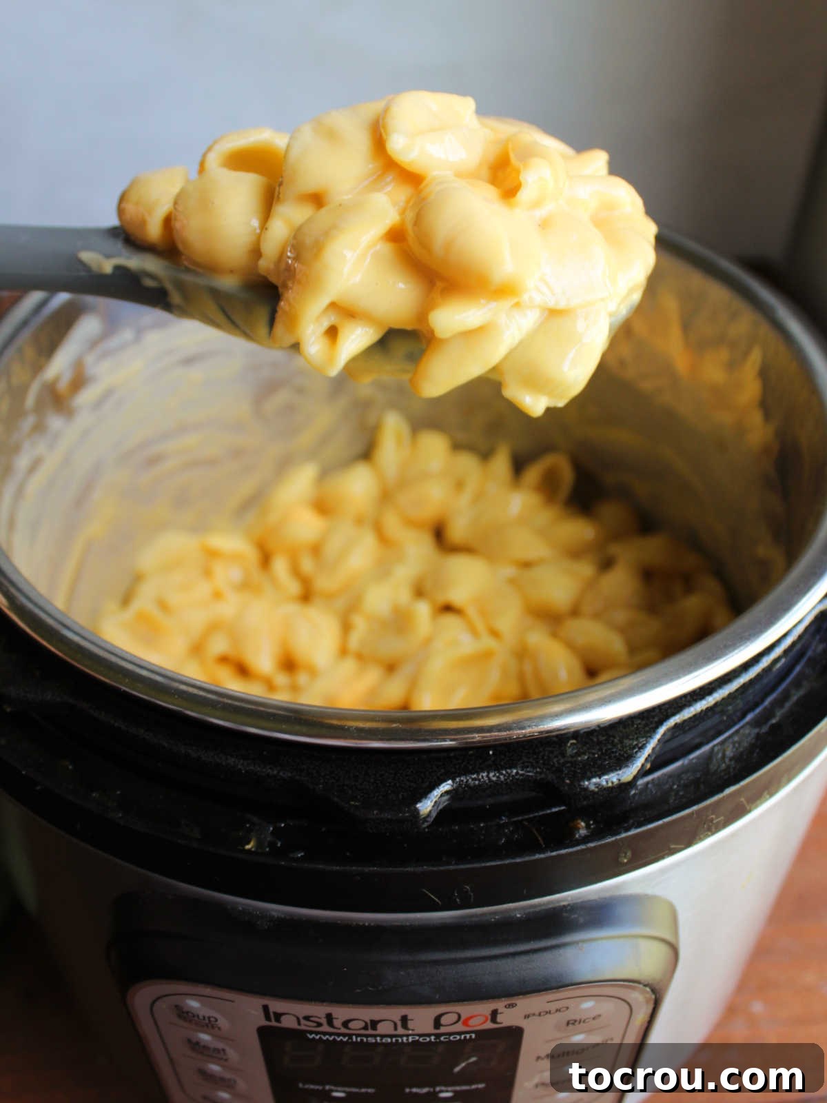 Serving spoon with a scoop of Instant Pot Shells and cheese showing the creamy cheese sauce and cooked pasta. 