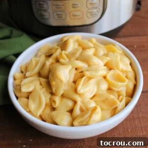 Close up of a bowl of creamy macaroni and cheese with shell shaped pasta and creamy velveeta cheese sauce in front of the Instant Pot it was made in.